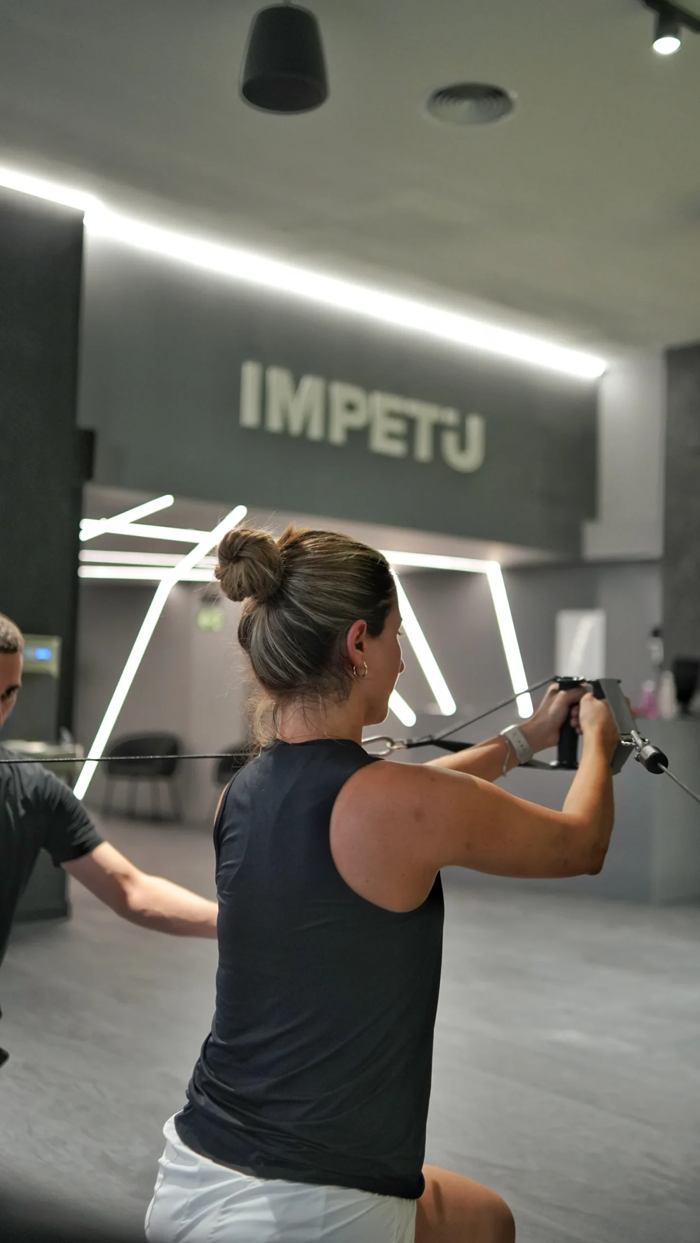 Clienta haciendo un ejercicio con poleas junto a su entrenador personal en Ímpetu